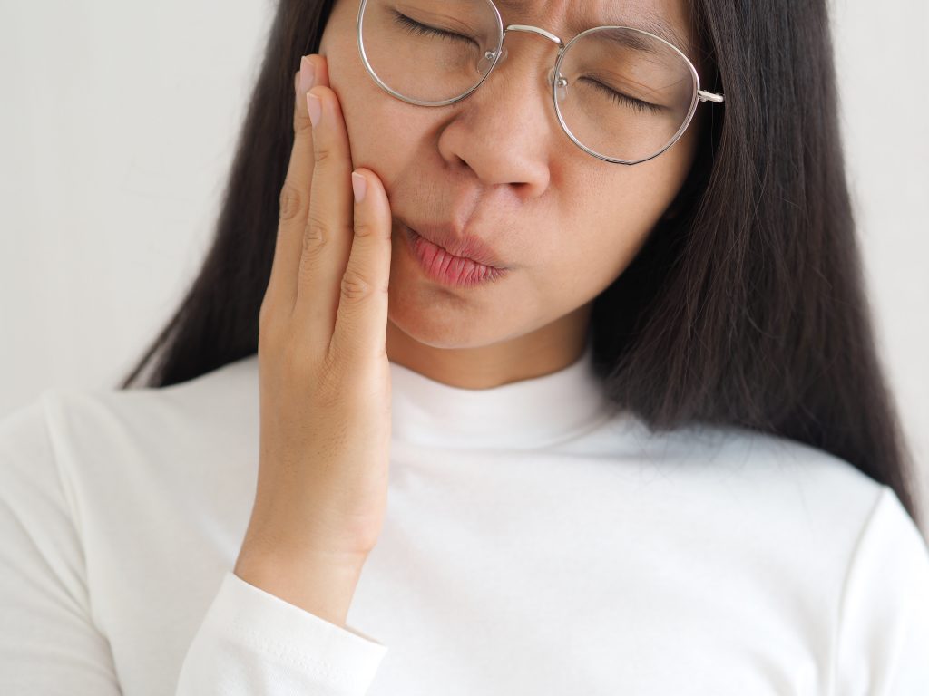 asian woman painfully grasping cheek in need of TMJ treatment