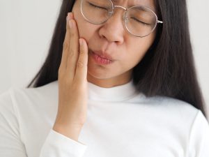 asian woman painfully grasping cheek in need of TMJ treatment